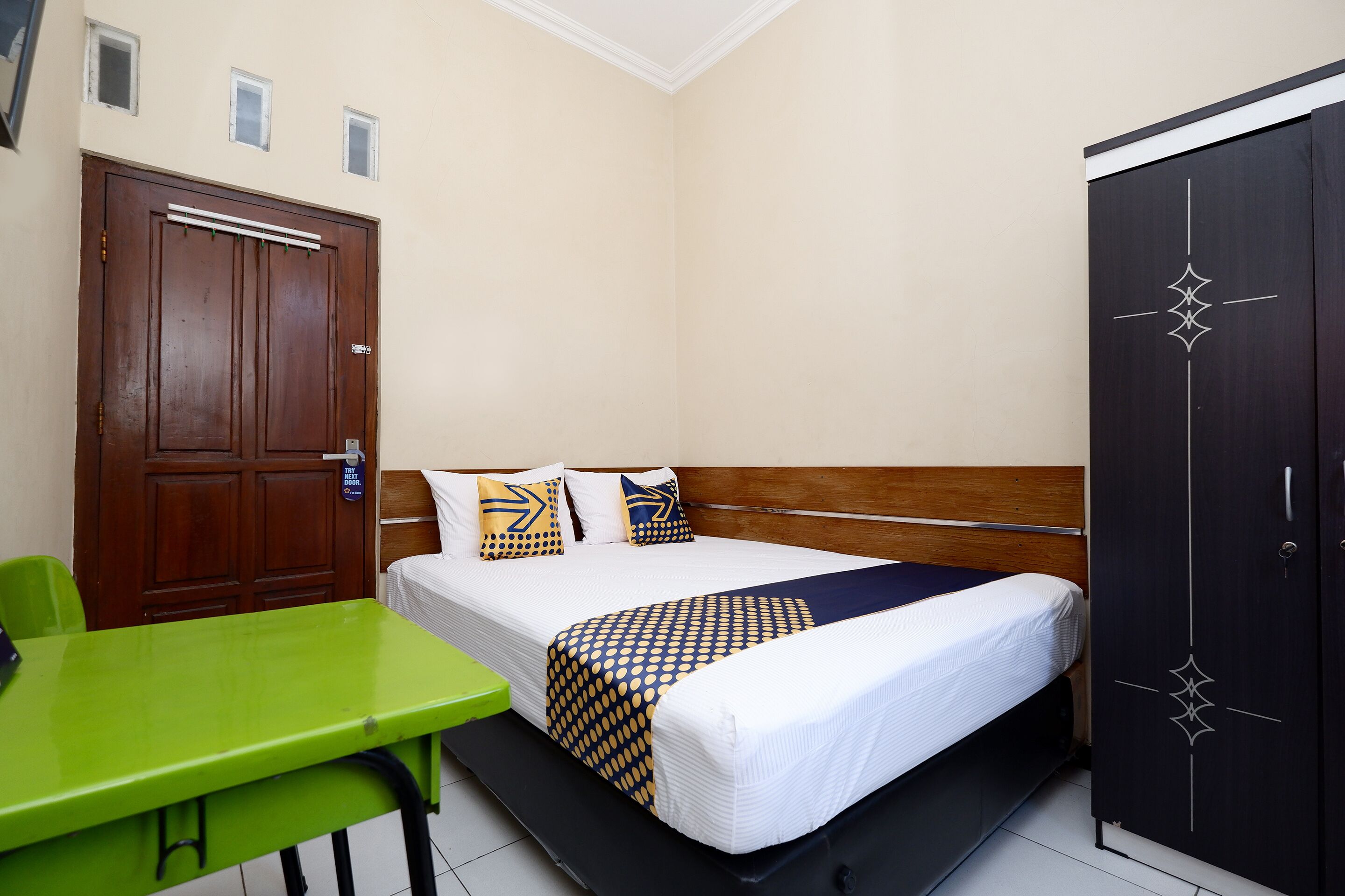 Une chambre d’hôtel avec un lit, une table verte, une armoire et une porte avec une pancarte.