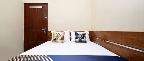 A hotel room with a wooden door, two pillows with geometric patterns, a blue and yellow bedspread, and a white bed.