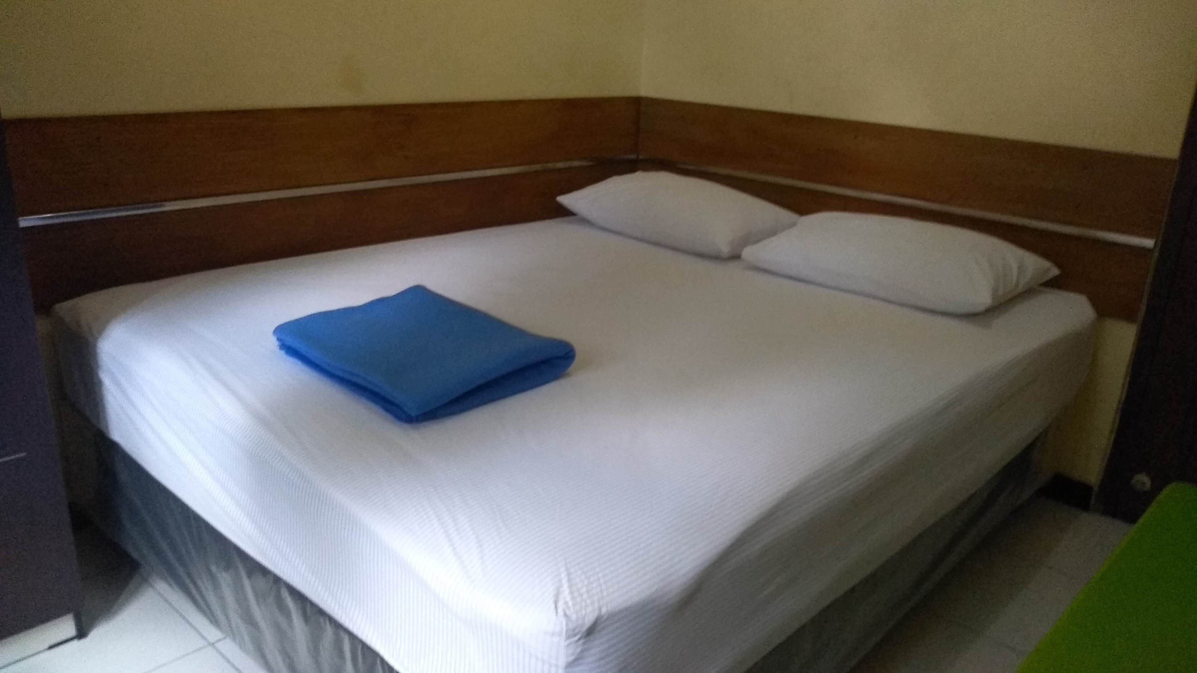 A single bed with a wooden headboard, white bedding, and a blue folded blanket.