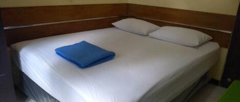A single bed with a wooden headboard, white bedding, and a blue folded blanket.