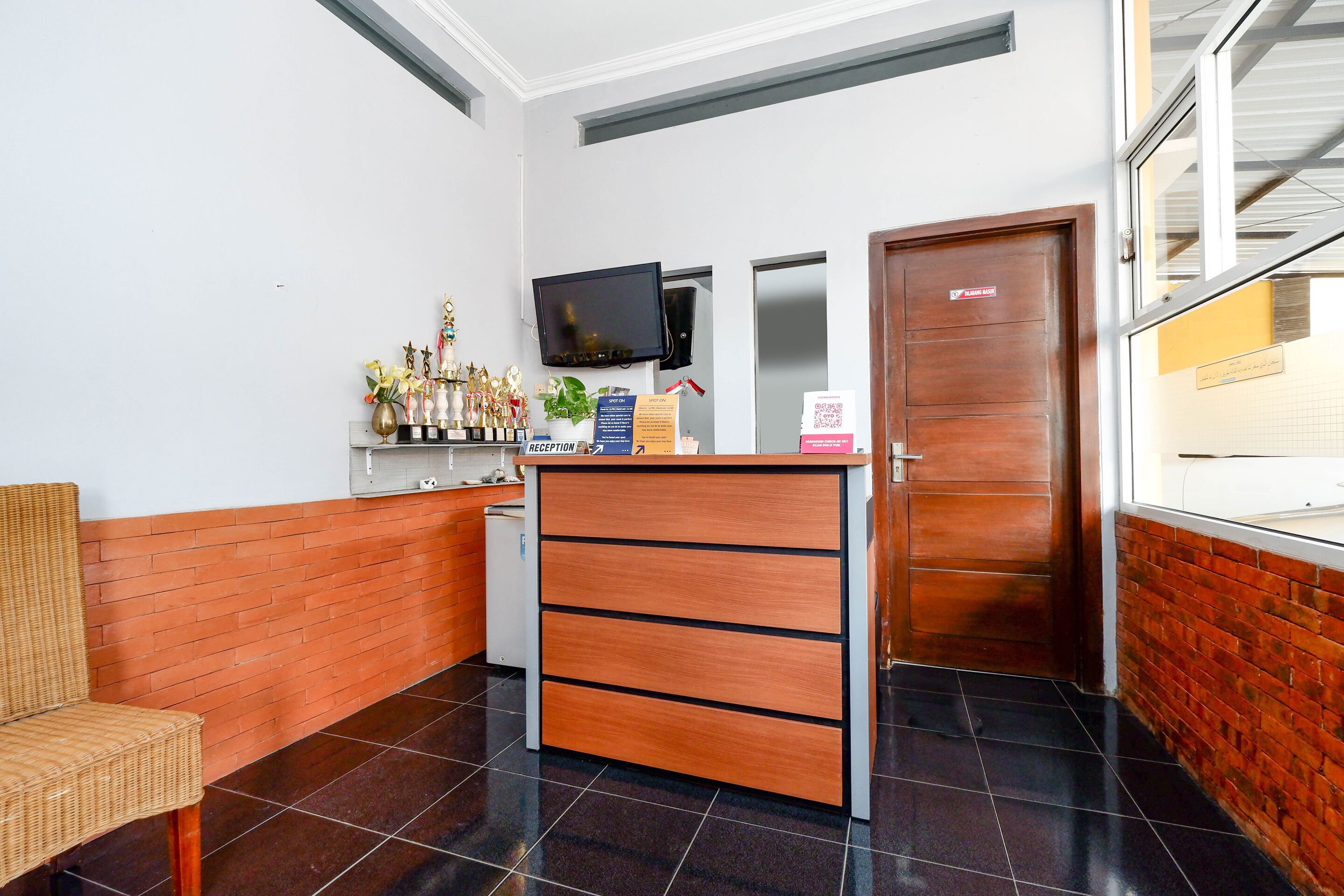 A reception area with a wooden desk, a television, a door, and a wicker chair.