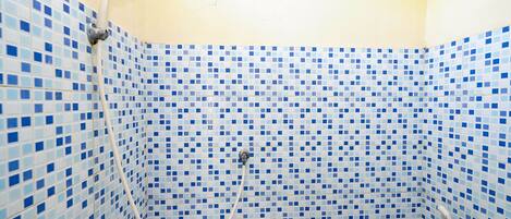 Un baño con zona de ducha revestida con azulejos, cabezal de ducha visible y ducha de mano.