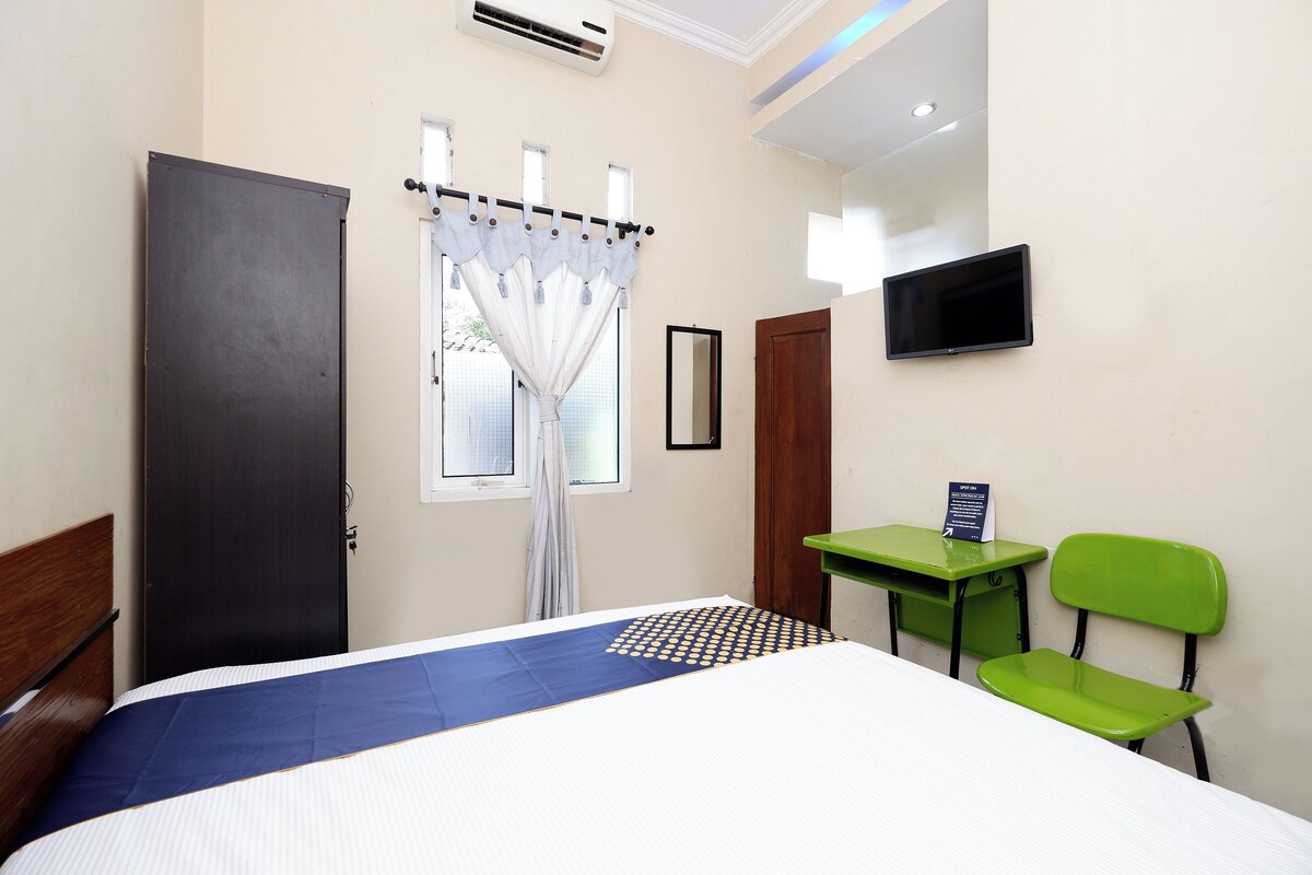 A hotel room with a bed, a desk, a chair, a TV, and a window with curtains.