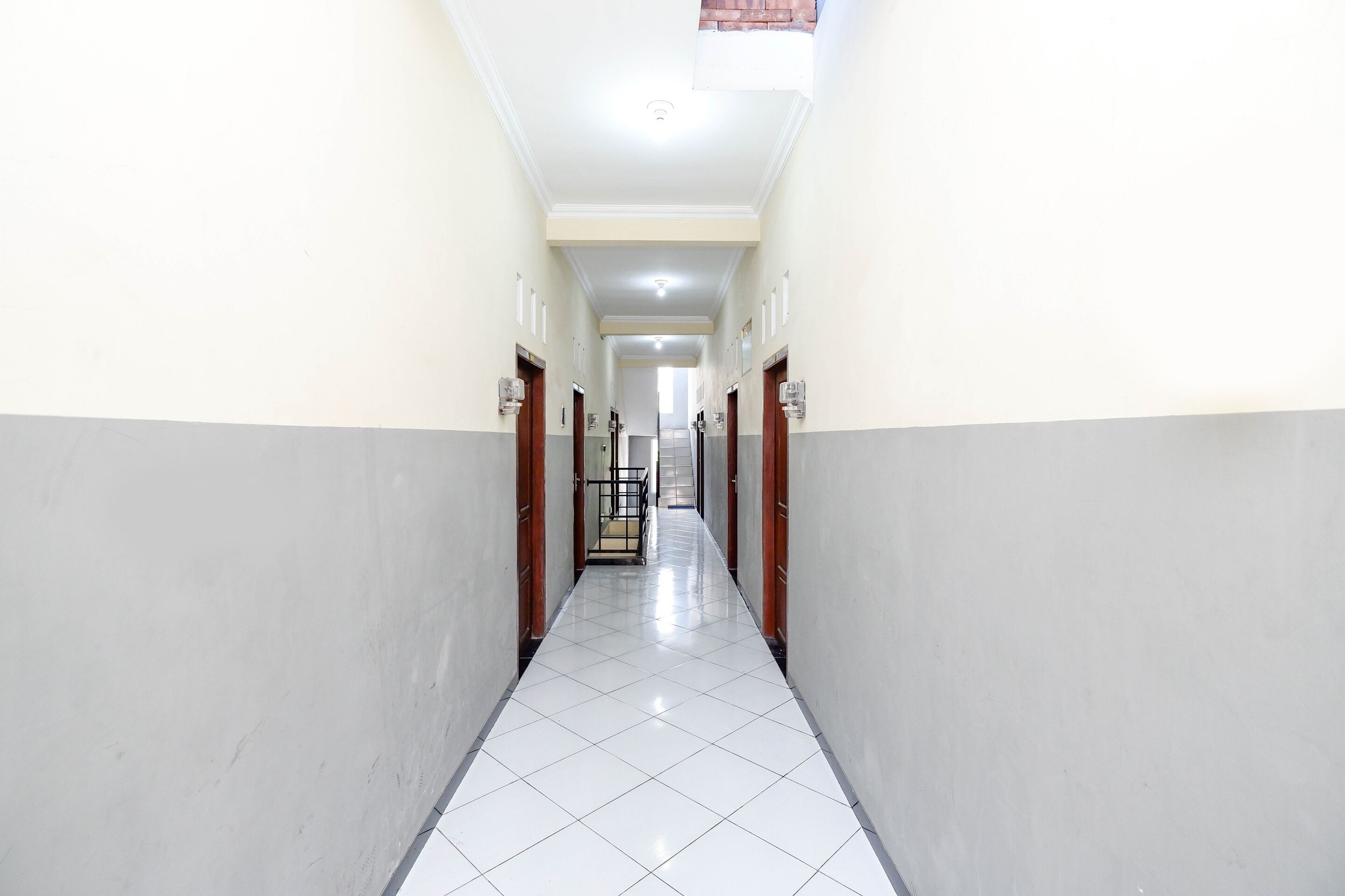 A long, narrow hallway with white tiled floors and light-colored walls, leading to a staircase.
