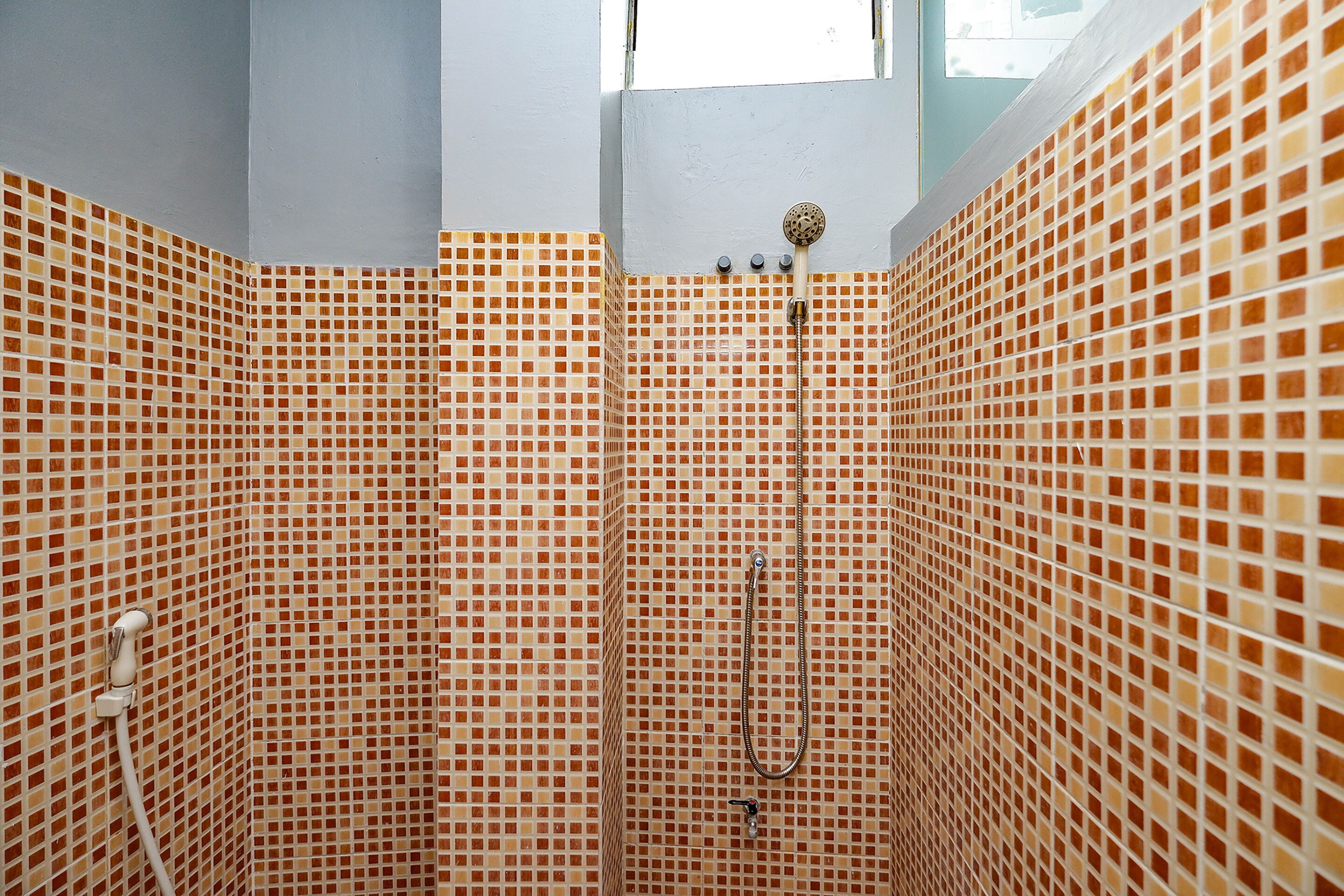 A bathroom with a shower area tiled with small, square, multicolored tiles.