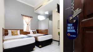 Une chambre d’hôtel avec deux lits, une fenêtre avec des rideaux, une porte avec une pancarte et un téléviseur fixé au mur.