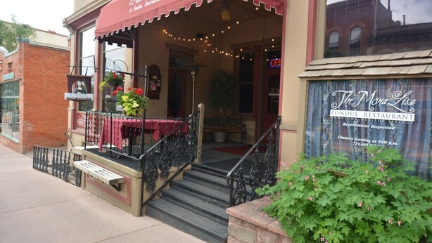 L’entrée d’un restaurant se distingue par un auvent rouge, des tables en terrasse et un escalier menant à la porte.