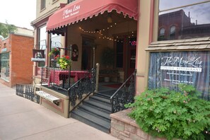 A restaurant entrance with a red awning, outdoor seating, and a staircase leading up to the door.