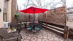 Un espace patio avec une table ronde et des chaises, un parasol rouge et un tapis à motifs.