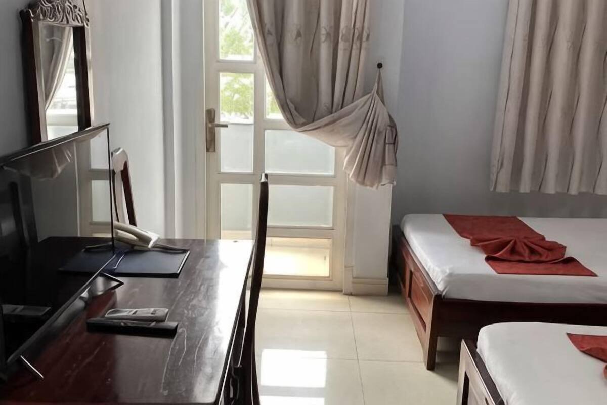 A hotel room with a bed, a desk with a computer, a television, and a window with curtains.