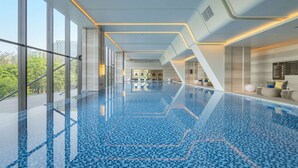 A modern indoor swimming pool with clear glass walls, a blue mosaic floor, and a view of greenery outside. - DoubleTree by Hilton Shenzhen Nanshan Hotel & Residences (Shenzhen)