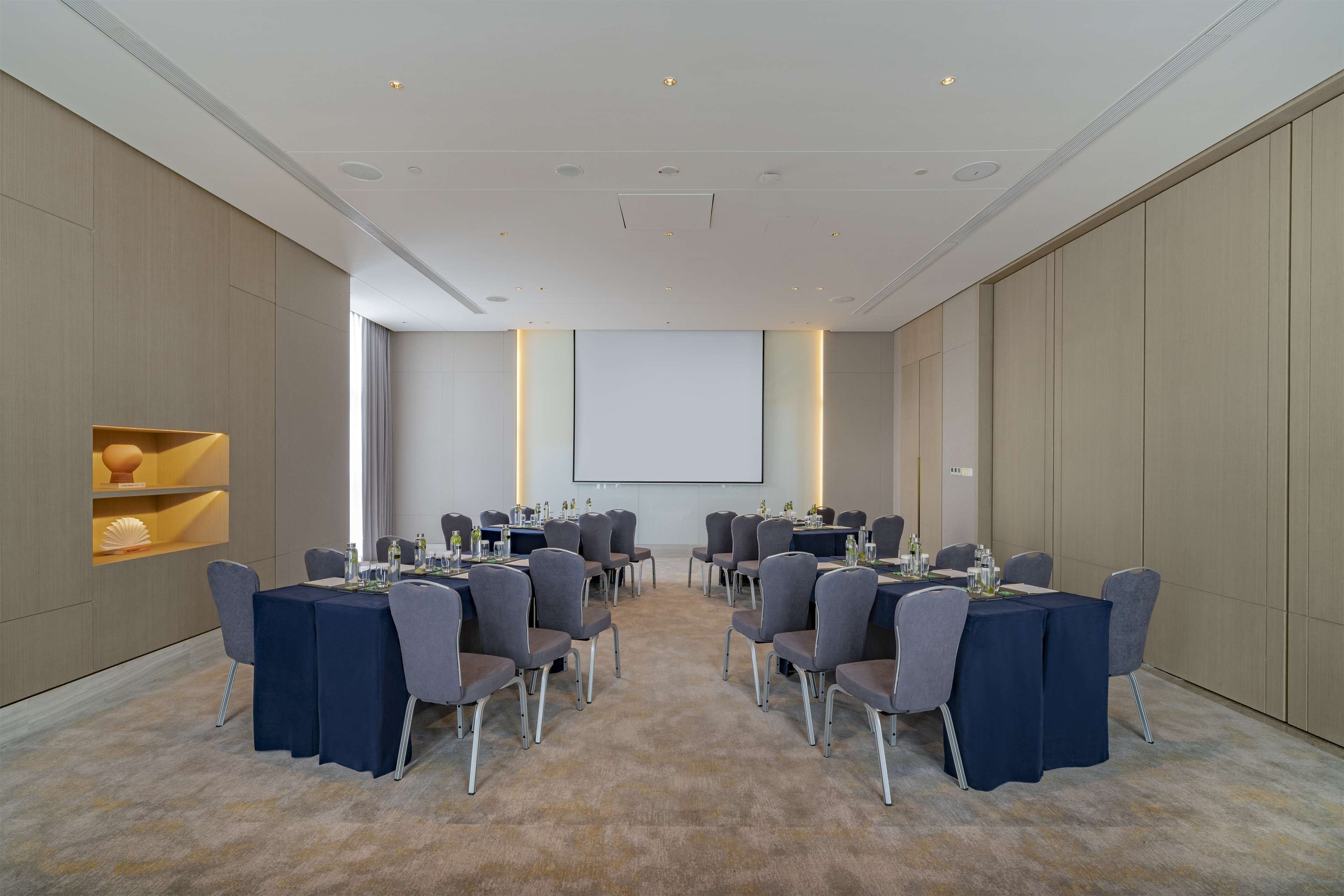 A conference room with tables and chairs, a projector screen, and a large window.