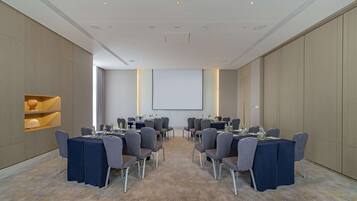 Uma sala de conferências com mesas e cadeiras, uma tela de projetor e um amplo janelão.