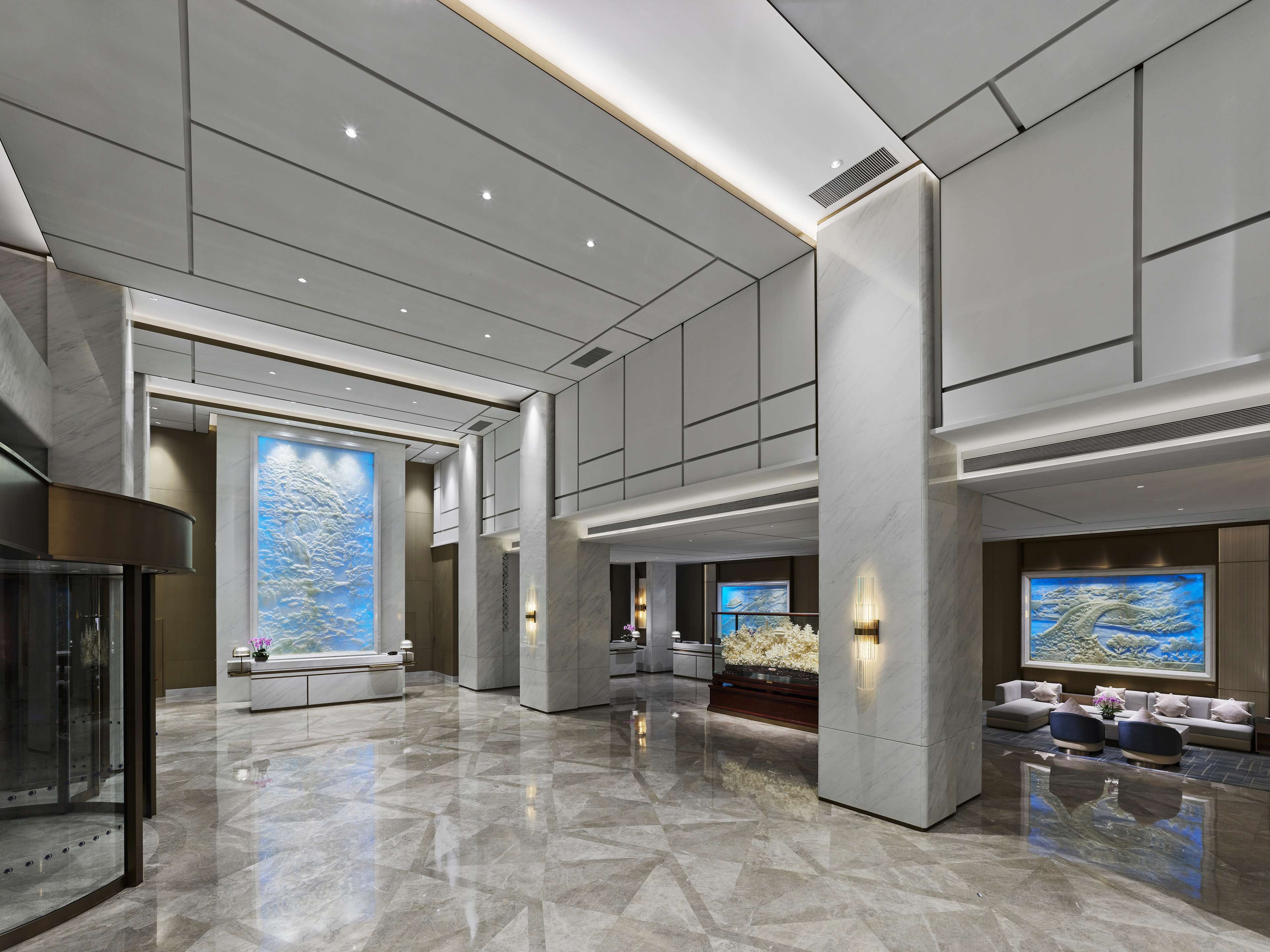A spacious lobby with a high ceiling, marble flooring, and large wall-mounted screens displaying nature scenes.