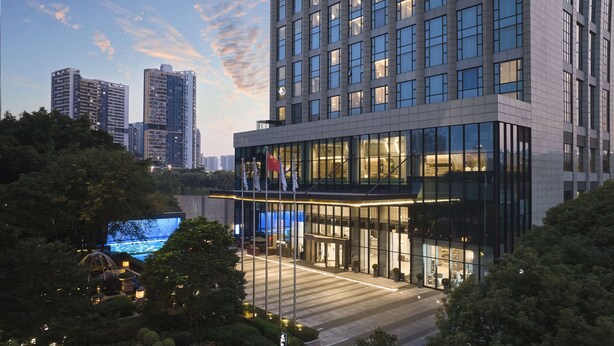 A modern hotel with a glass facade, multiple floors, and a flag on the roof. - DoubleTree by Hilton Shenzhen Nanshan Hotel & Residences (Shenzhen)