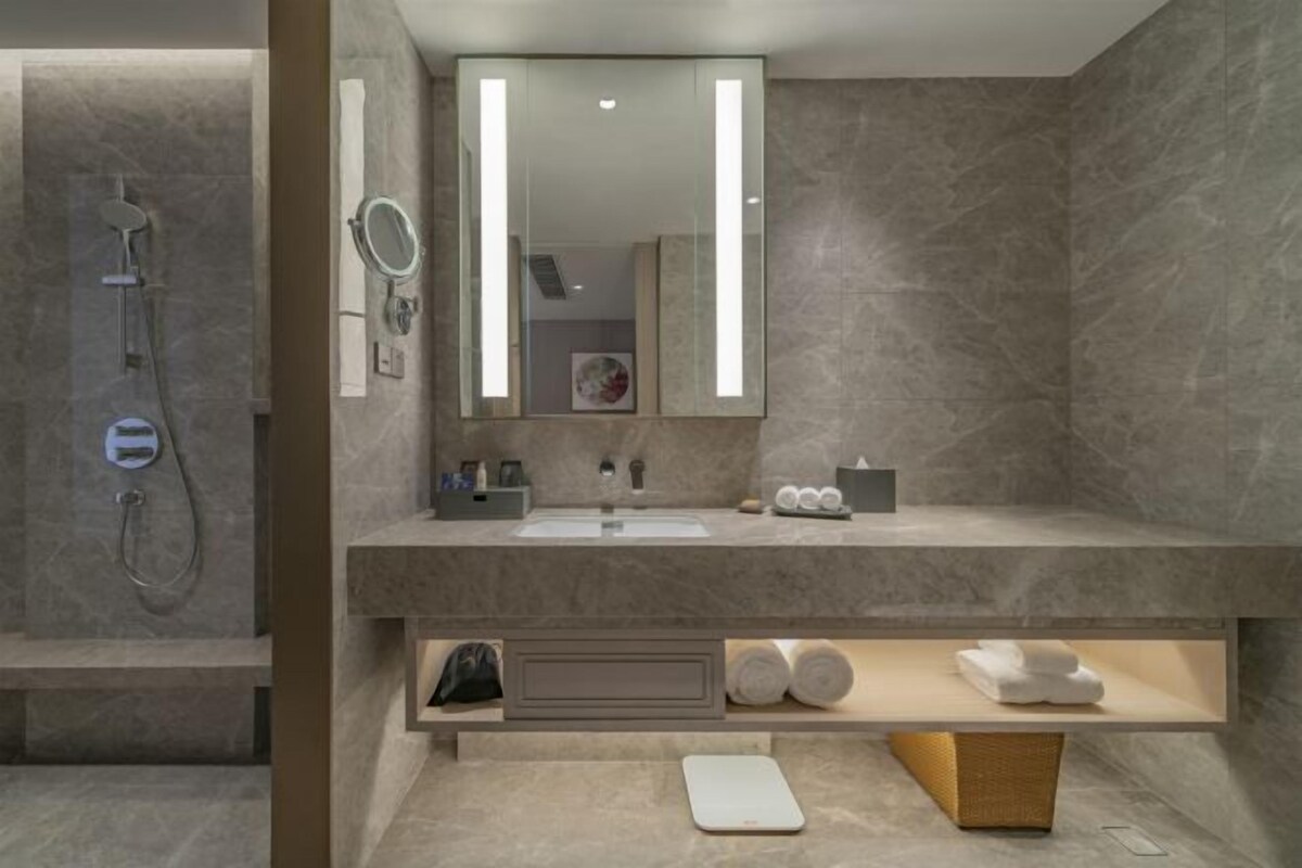 A modern bathroom with a large mirror, a shower, and a vanity with a sink and towel storage.