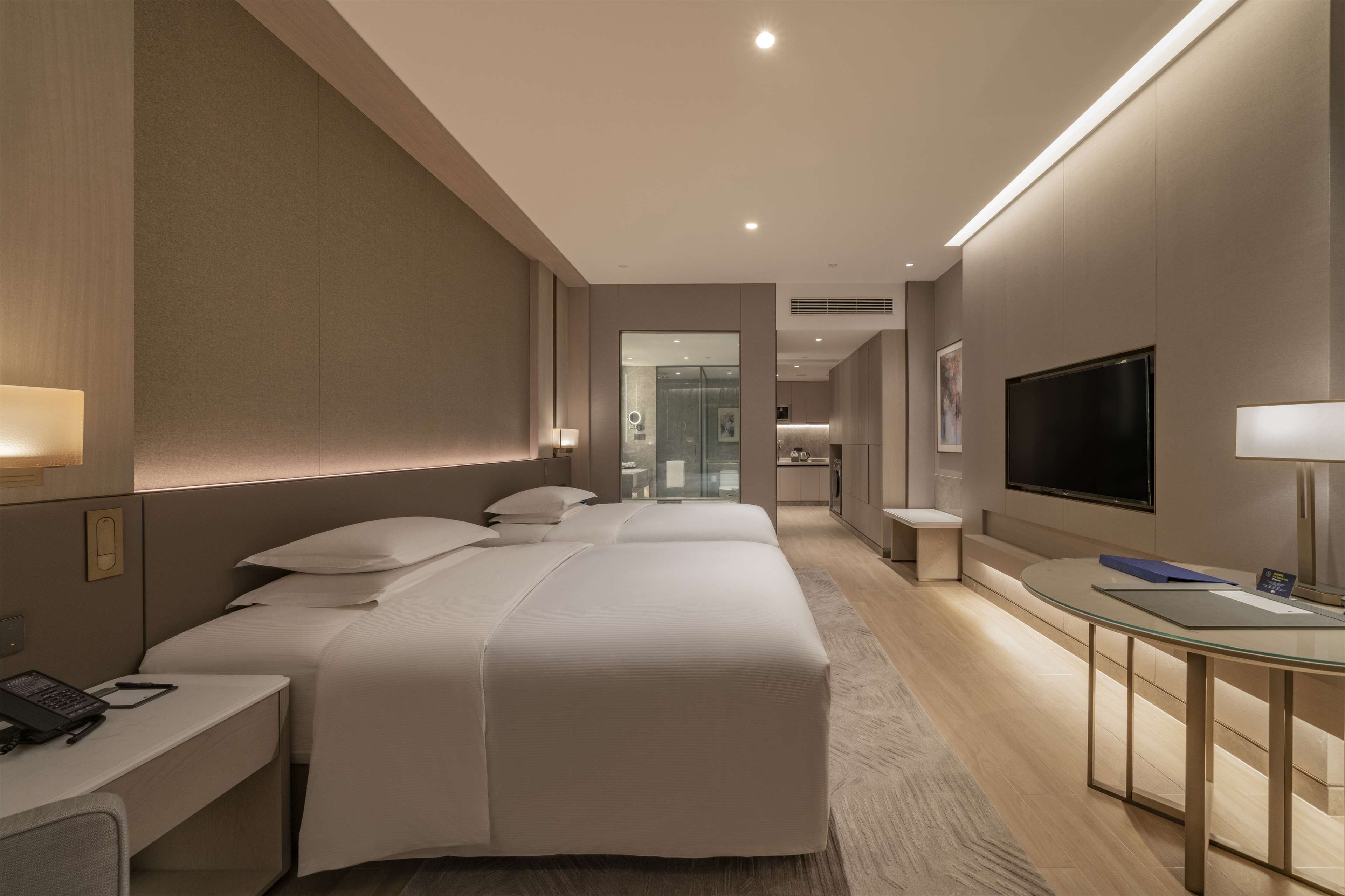 Una camera d'albergo moderna con un letto grande, comodini, una TV e un tavolino da caffè in vetro.