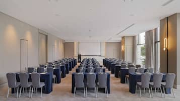 A conference room with rows of tables and chairs, a projector screen, and large windows.
