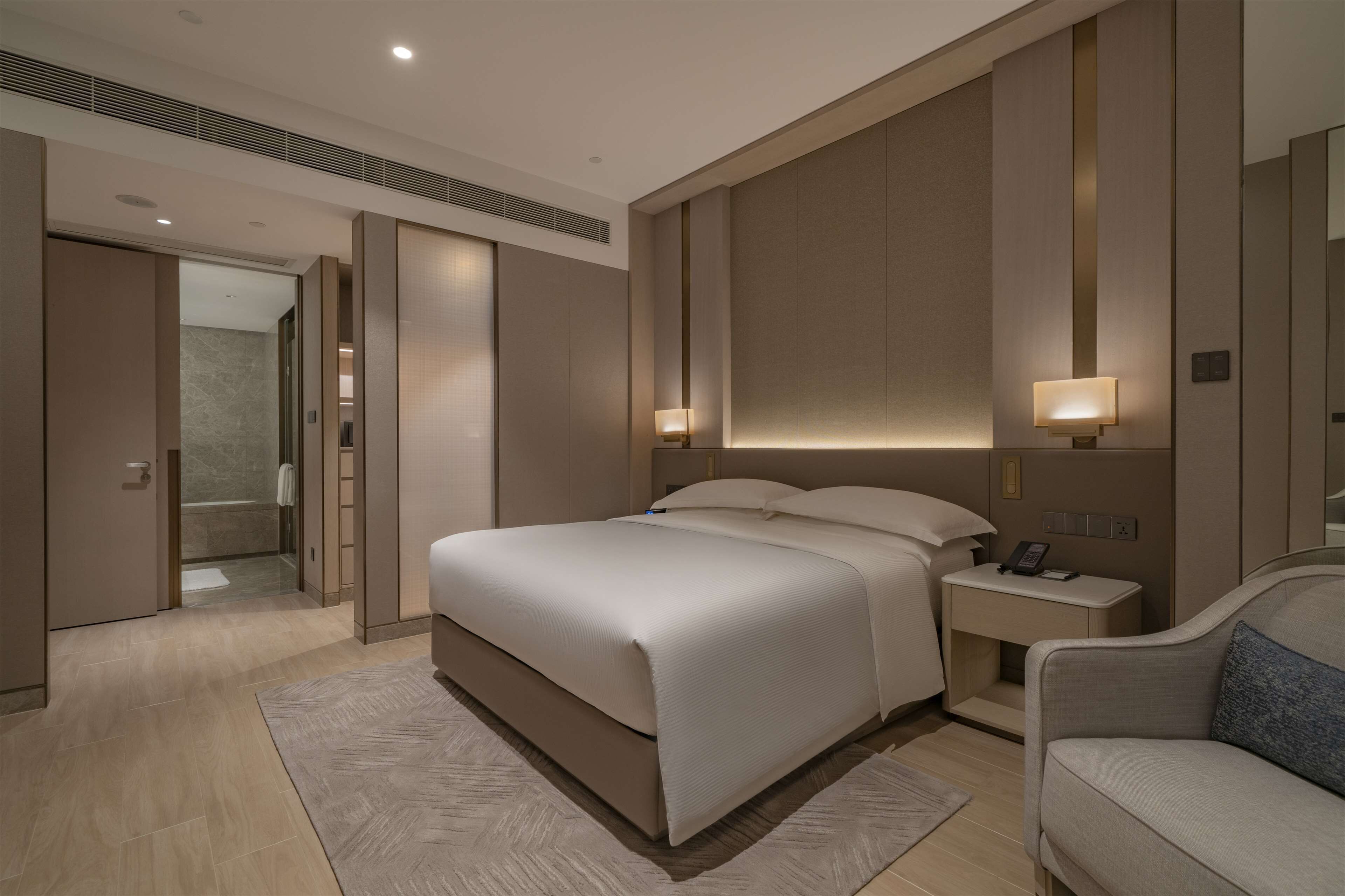 A modern hotel room with a large bed, bedside tables, a nightstand, a sofa, and a walk-in closet.