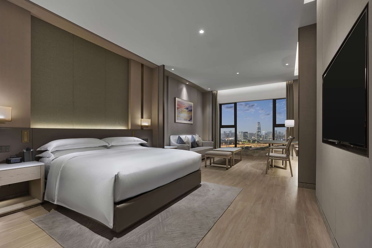 Ein modernes Hotelzimmer mit einem großen Bett, Nachttischen, einem Schreibtisch und Blick auf die Stadt.