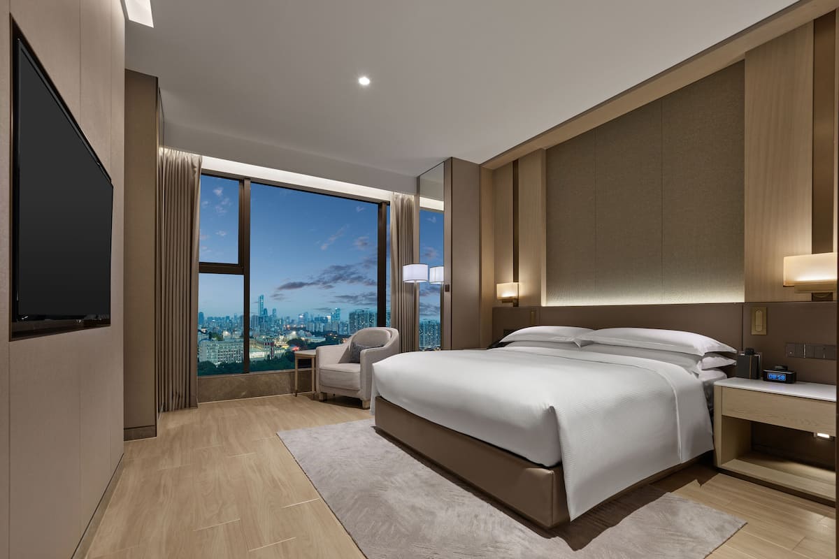 Ein modernes Hotelzimmer mit einem großen Bett, einem Schreibtisch, einem Sessel und einem Fernseher.