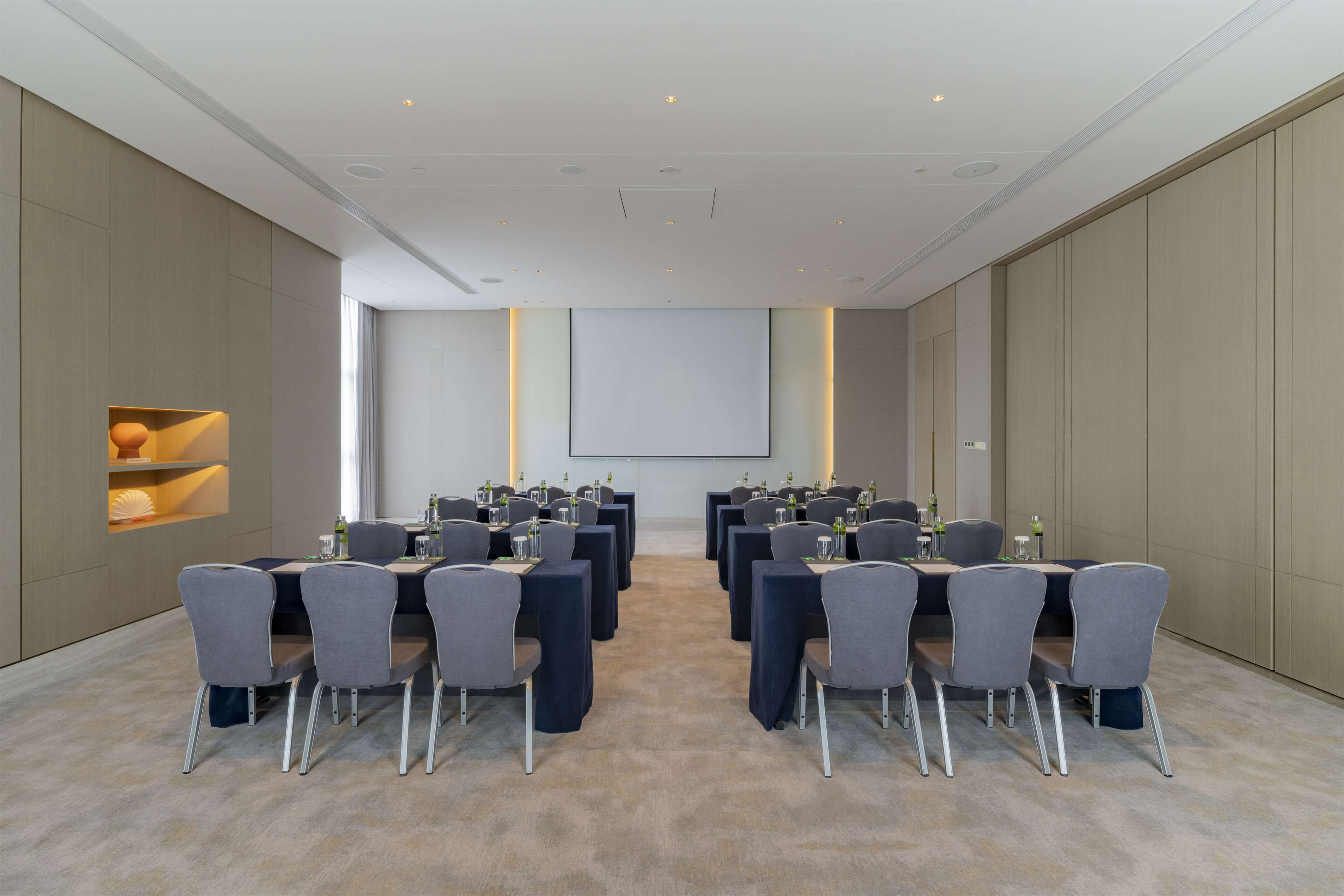Un salón de conferencias con varias mesas y sillas, una pantalla de proyector y suelo alfombrado.