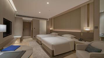 A hotel room with two beds, a sofa, a desk with a phone, and a TV.