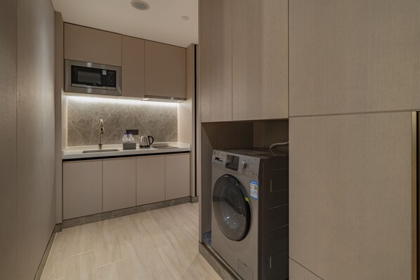 A modern kitchen with a built-in microwave, a washing machine, and a stainless steel sink.
