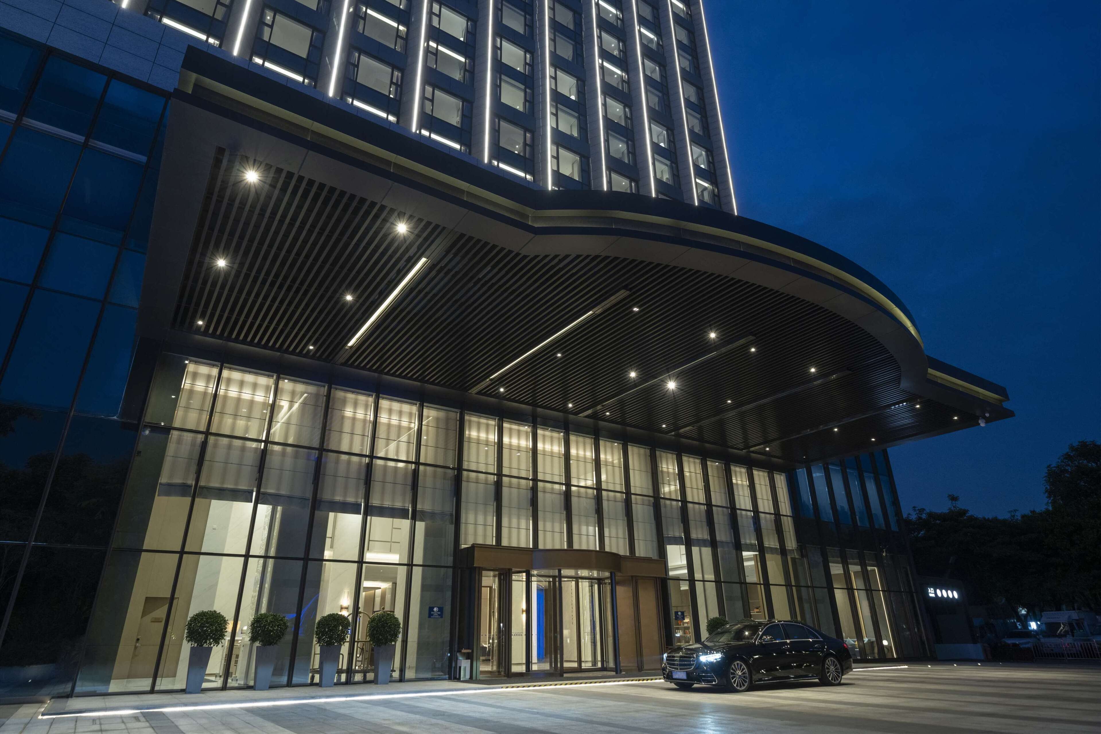 A modern hotel with a curved entrance, large glass windows, and a car parked in front.
