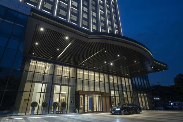 A modern hotel with a curved entrance, large glass windows, and a car parked in front.