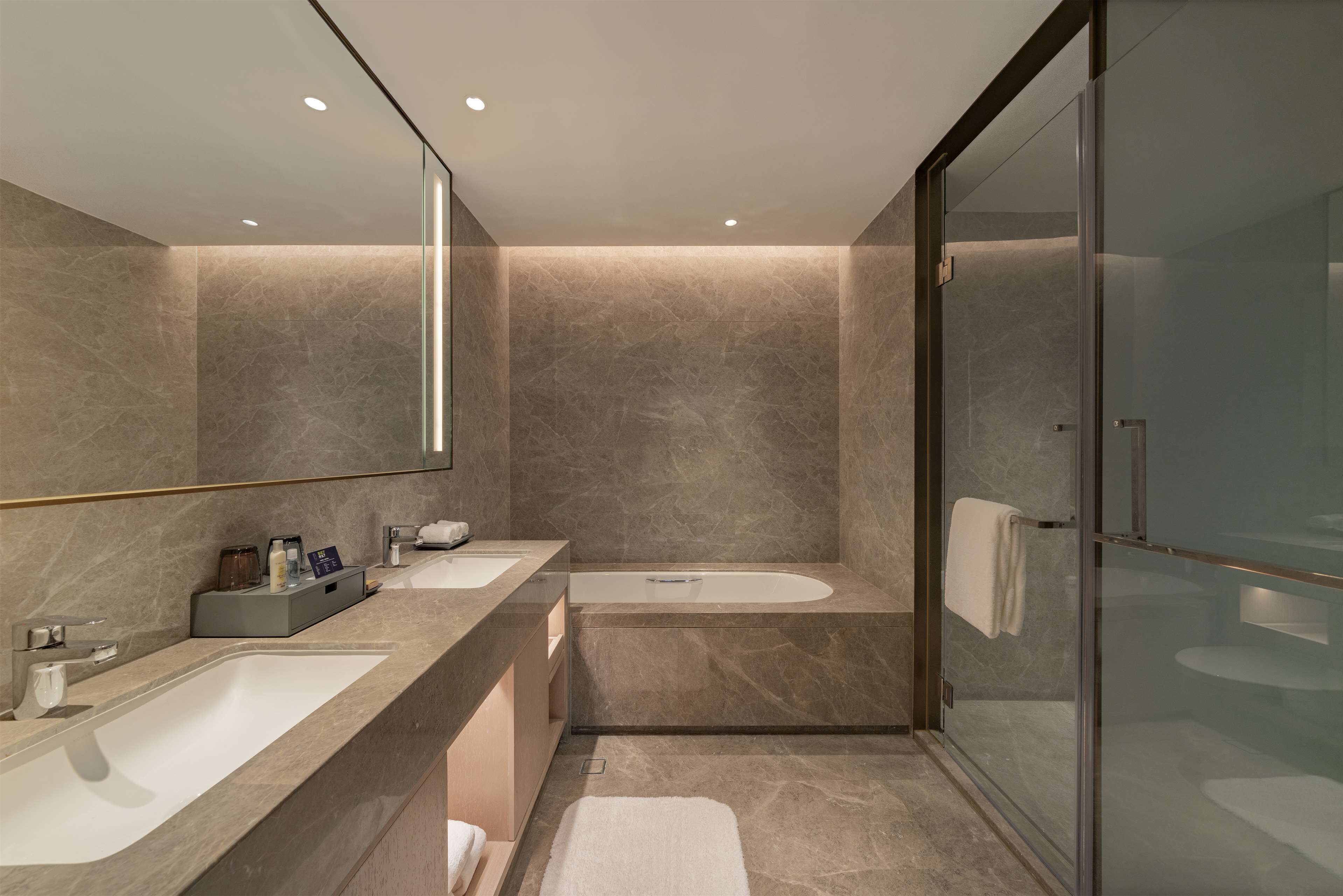 A modern bathroom with a large mirror, two sinks, a bathtub, and a glass shower enclosure.