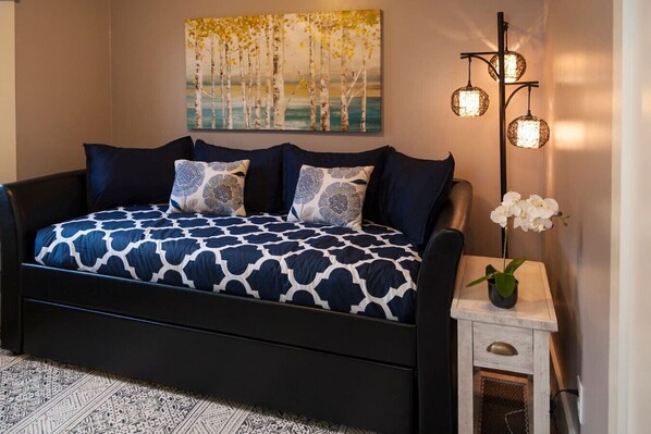 Een slaapkamer met een zwart bed, beddengoed met een patroon, een schilderij van bomen, en een vloerlamp met drie lampen.