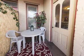 Relax in this serene outdoor seating area with a round table and two chairs, surrounded by lush greenery and a cozy lantern.