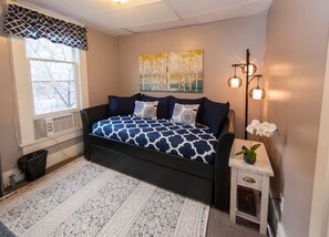 Een slaapkamer met een bed, een klein tafeltje met een orchidee en een schilderij aan de muur.