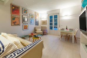A modern living room with a sofa, a dining table with chairs, a TV, and various framed artworks on the walls. - Cervo Piccolo Incanto Flat with Balcony, Cervo, Italy (Cervo)