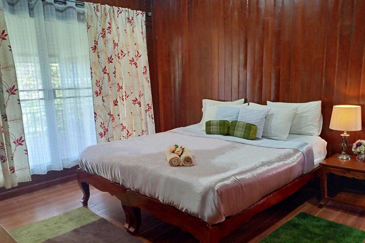 A neatly made bed with a white and pink bedspread, two green pillows, and a rolled towel on the bed.