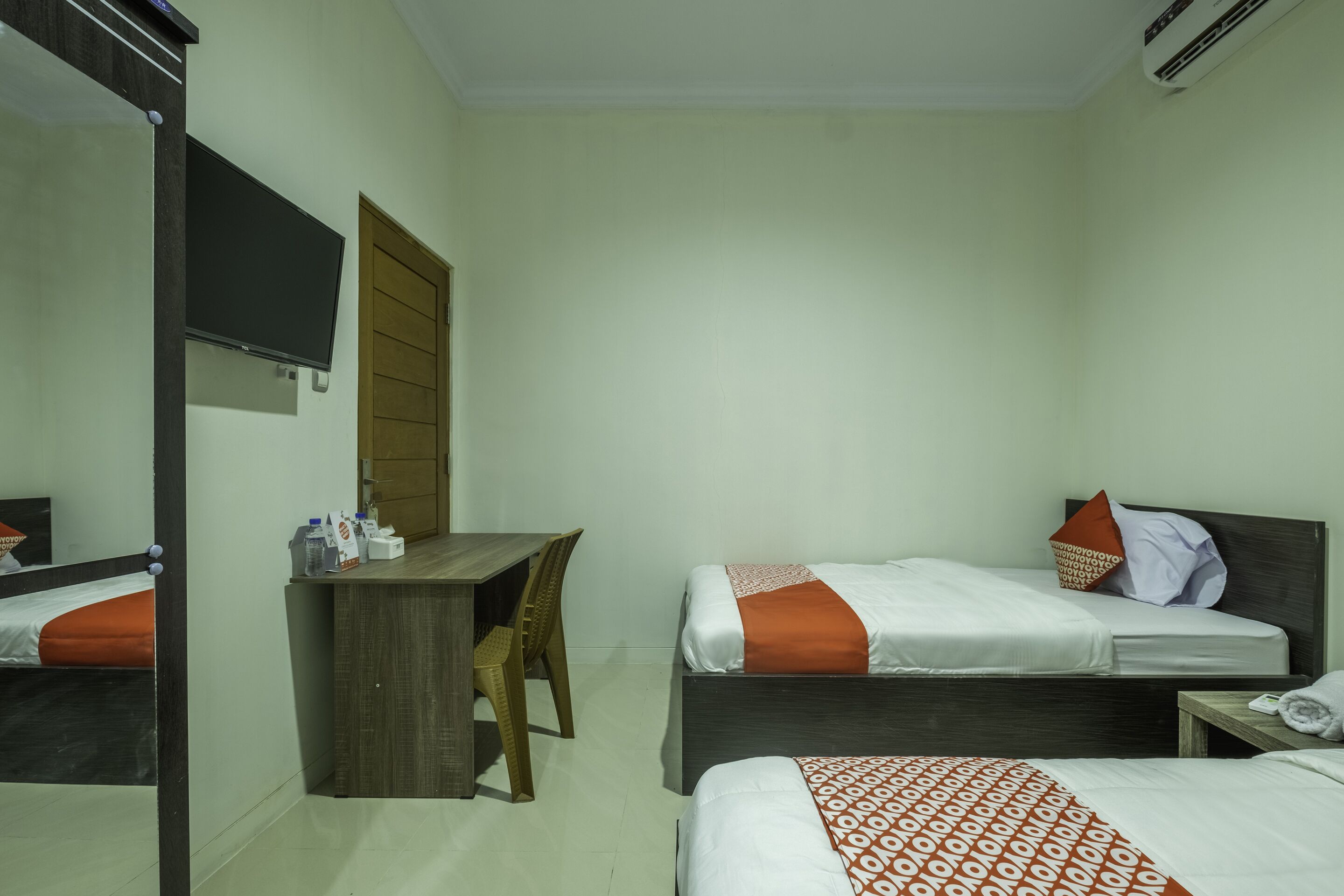A hotel room with two beds, a desk, a chair, and a mirror.