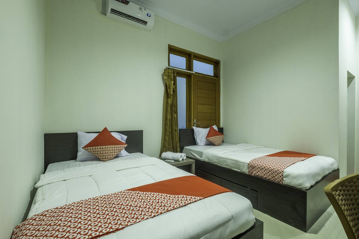 A hotel room with two beds, a window with curtains, a bedside table, and a chair.