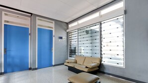 A waiting area with a blue door, a beige sofa, and a glass partition. - SPOT ON 2281 Omajo (Semarang)