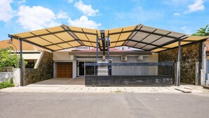 A covered driveway leading to a house with a stone facade and a metal gate. - SPOT ON 2281 Omajo (Semarang)