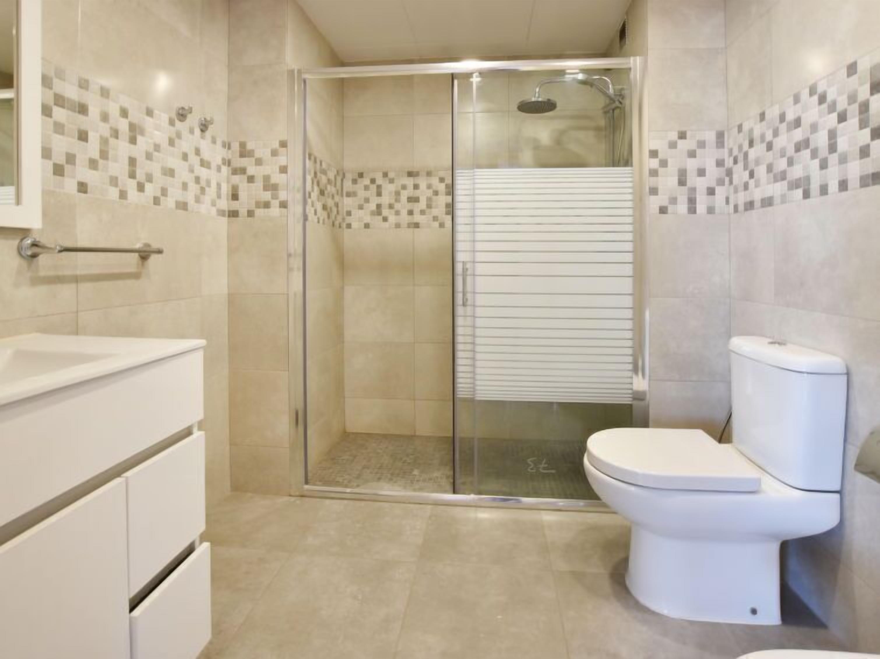 A modern bathroom with a glass-enclosed shower, a white toilet, and a vanity with drawers.