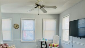 A living room with a sofa, a small table, a child’s chair, a television, and a ceiling fan. - Beach Block, Renovated 2 bdrm, sleep 6, 2nd Flr unit Parking and 4 beach badges (Seaside Park)