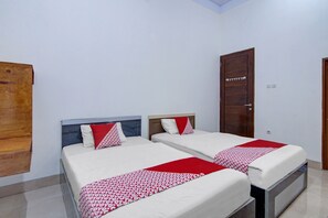 Ein Hotelzimmer mit zwei Betten, jeweils mit weißer Bettwäsche und roten Akzenten, einer Holztür und einer weißen Wand.