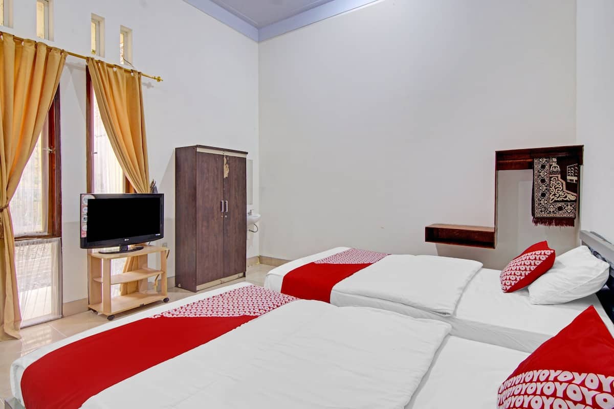 Une chambre d’hôtel avec deux lits, un téléviseur posé sur un meuble en bois, une armoire et une petite table.