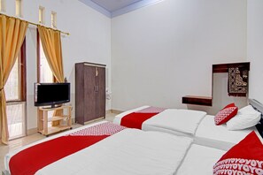 Ein Hotelzimmer mit zwei Betten, einem Fernseher auf einem Holzgestell, einem Kleiderschrank und einem kleinen Tisch.