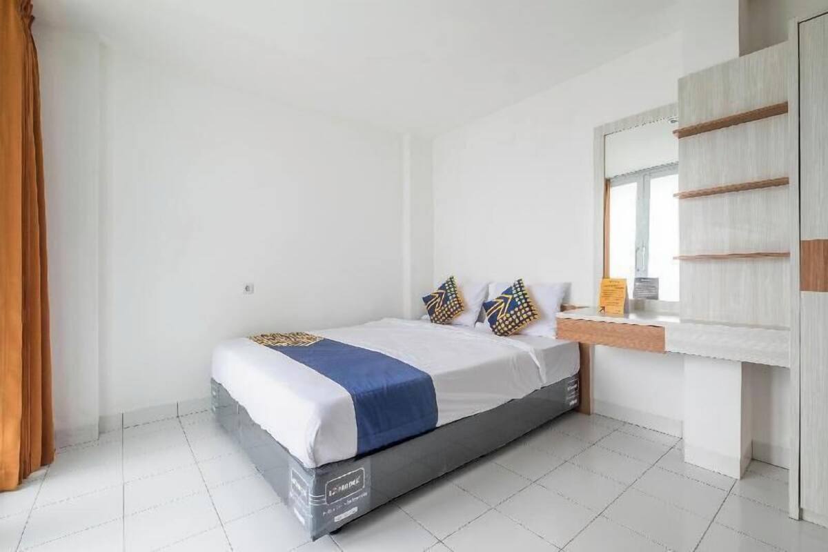 A hotel room with a bed, a bedside table, a mirror, and a window.