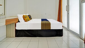Una camera d'hotel con un letto, un comodino in legno, uno specchio e una porta scorrevole in vetro con tende.