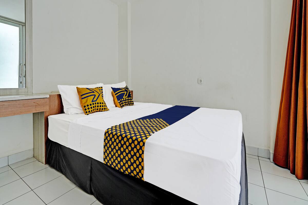 A hotel room with a bed, a nightstand, and a window.