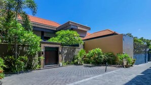 A residential area with a paved driveway, a house with a red-tiled roof, and surrounding greenery. - OYO 2143 Leluhur Bali Apartment (Keroboken Kelod)