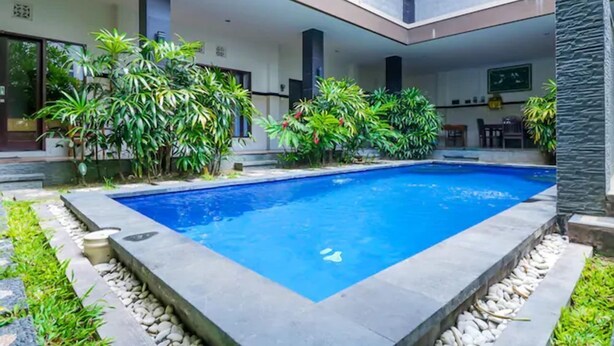 A modern pool area with a rectangular pool, surrounded by lush greenery and stone accents. - OYO 2143 Leluhur Bali Apartment (Keroboken Kelod)